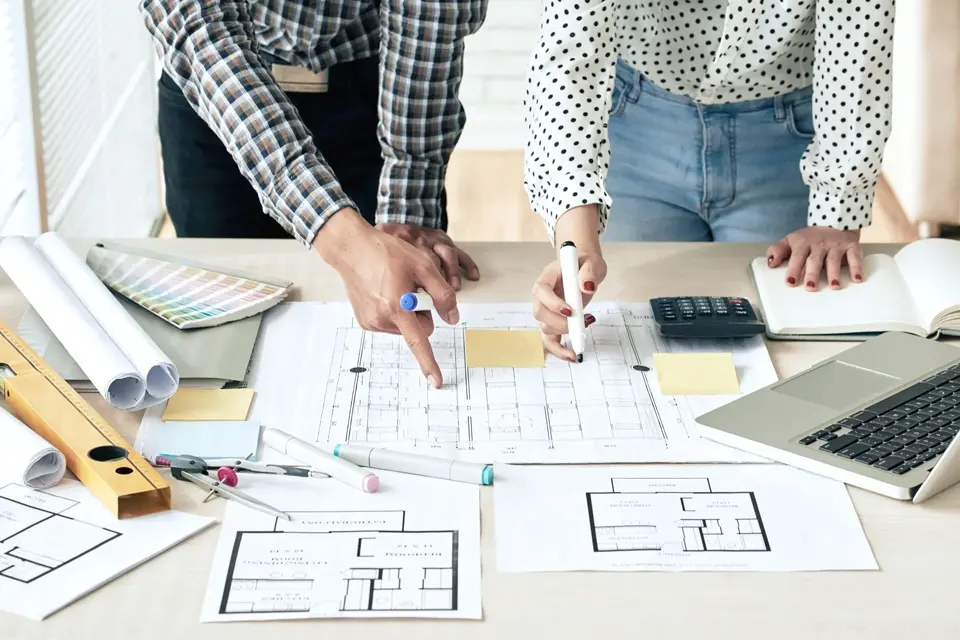 Dos ingenieros / arquitectos revisando un plano sobre una mesa de trabajo